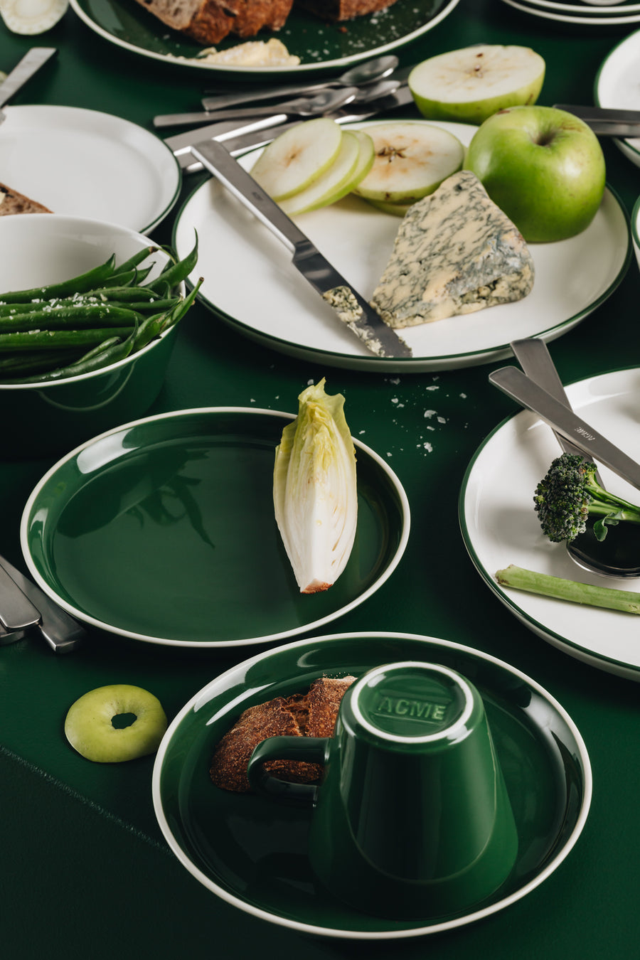 Green and white Acme tableware, some with food on, placed on a green counter