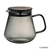 Smoky gray glass coffee server with black handle and lid on a white background, featuring the Hario logo.