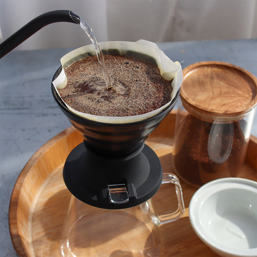 Coffee being brewed with a pour-over coffee maker Hario Switch V60 Immersion Dripper on a wooden tray.